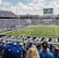 A large football stadium filled with fans watching a live game. Players are on the field, and the atmosphere is lively with a full audience. The scoreboard displays the action, and banners for the Kentucky Wildcats are visible.