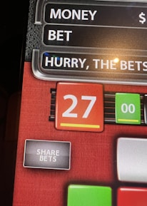 A digital display screen showing a casino betting interface, with text prompting to hurry bets and a highlighted number 27 in red. There are options for betting amounts and a 'share bets' button.