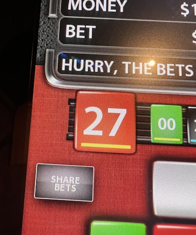 A digital display screen showing a casino betting interface, with text prompting to hurry bets and a highlighted number 27 in red. There are options for betting amounts and a 'share bets' button.